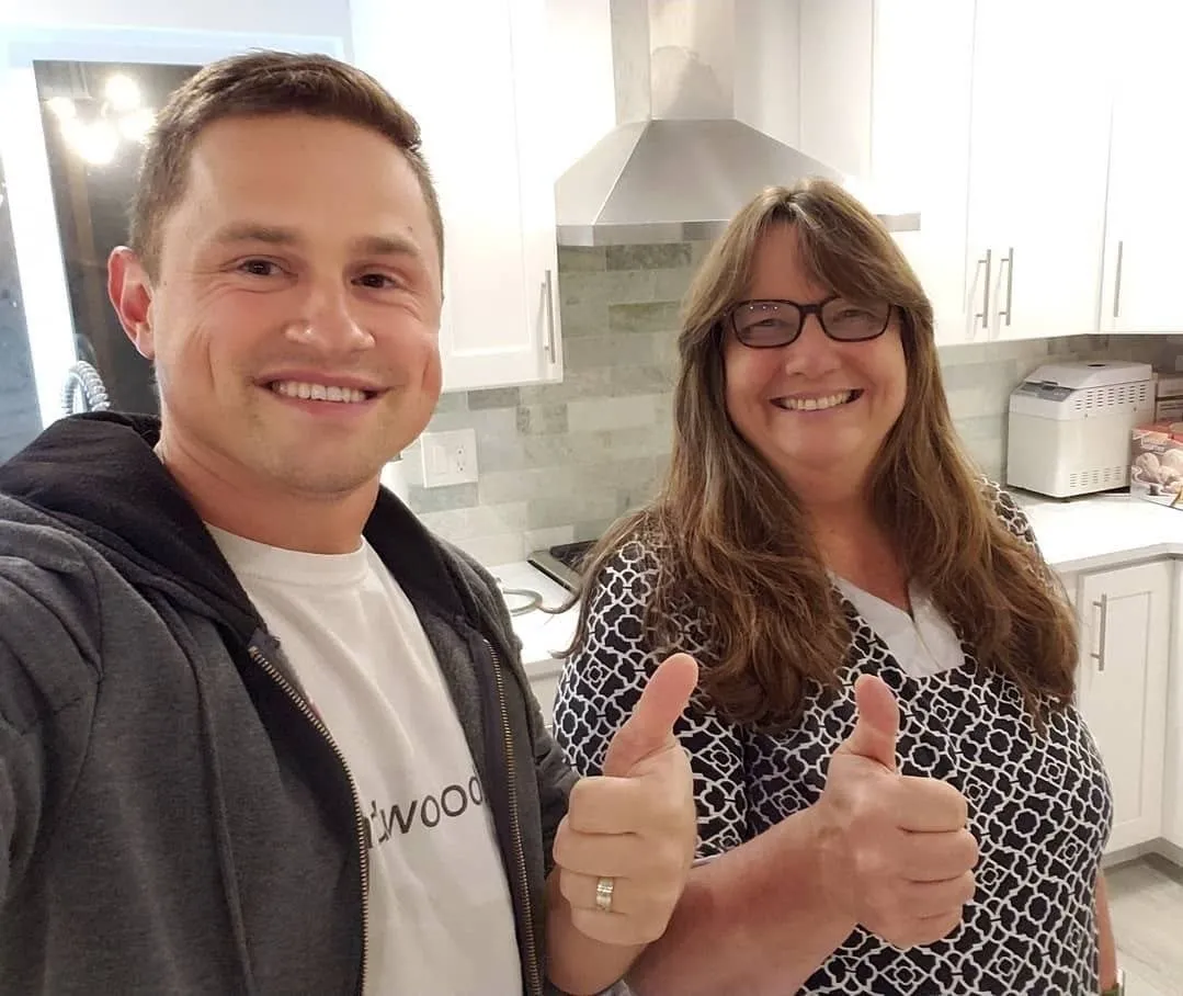 A Vision Flooring team member and a smiling homeowner giving two thumbs up in a kitchen