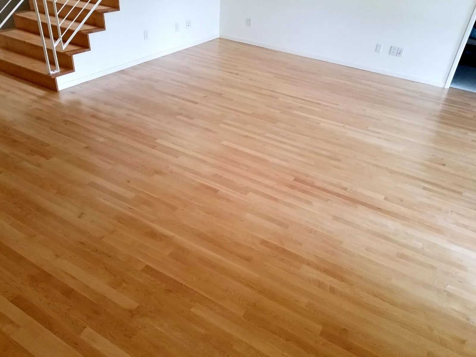 New light hardwood floor in a room beside a staircase