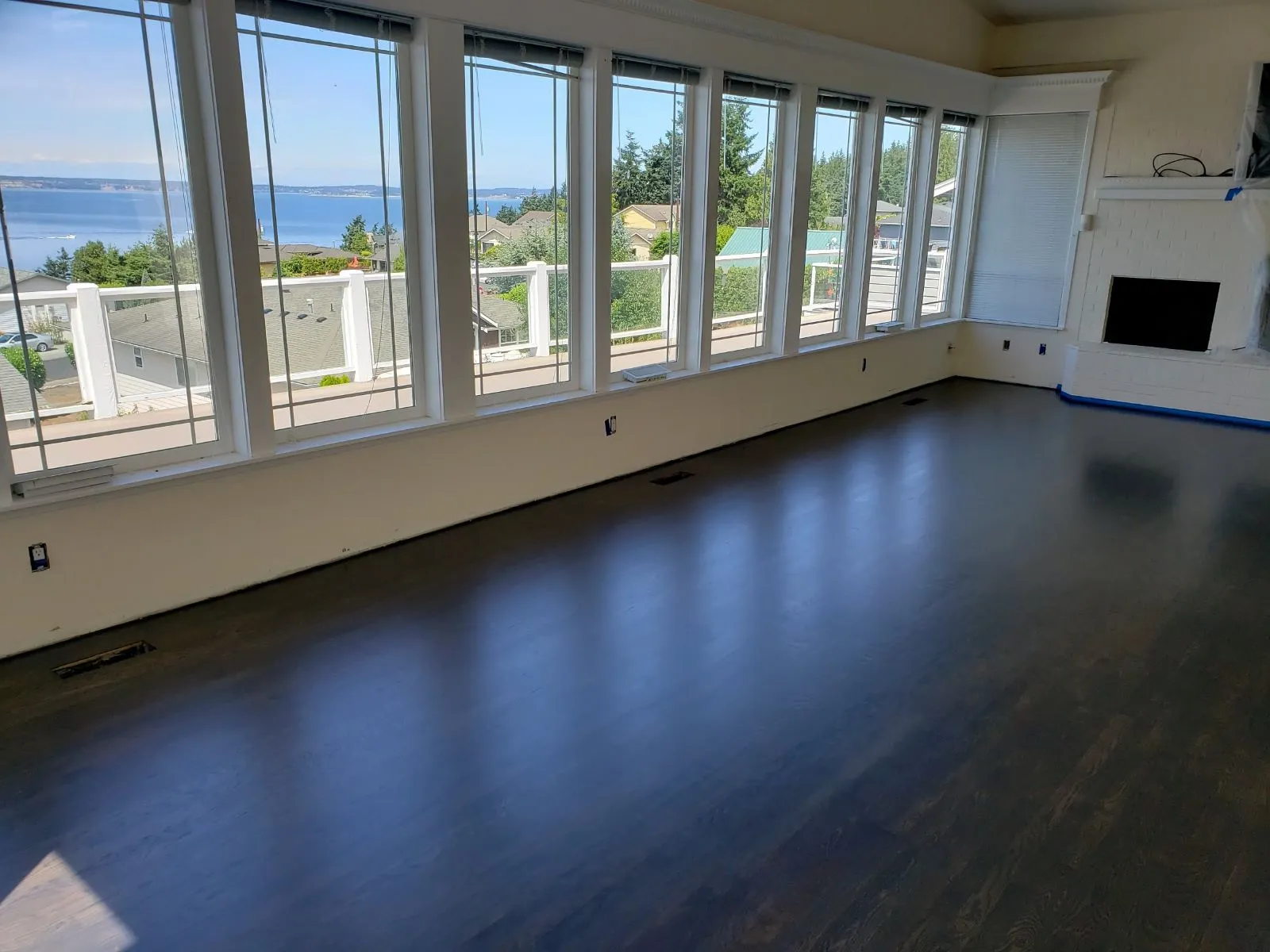 Dark hardwood floor in an empty room with large windows overlooking the water