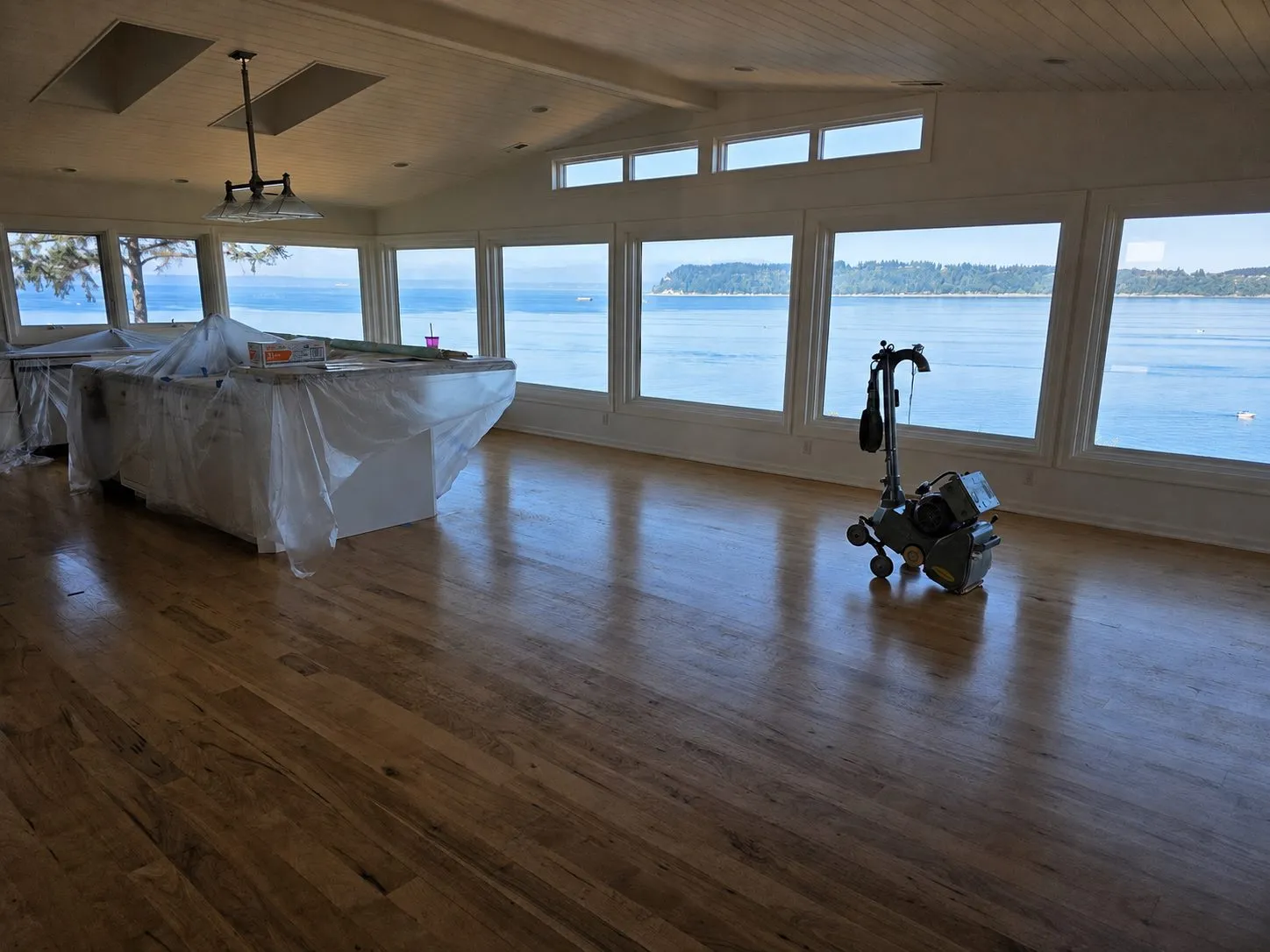 Hardwood floor during refinishing, with a floor sander in the room