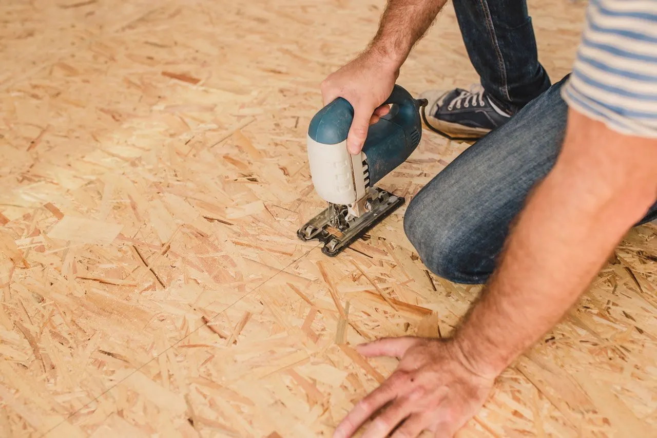 A person cutting a plywood subfloor with a jigsaw