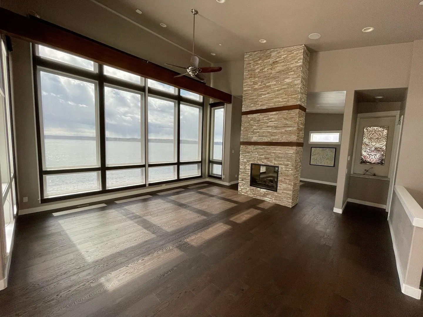 Dark hardwood floor in a living room with a stone fireplace and tall windows over the water