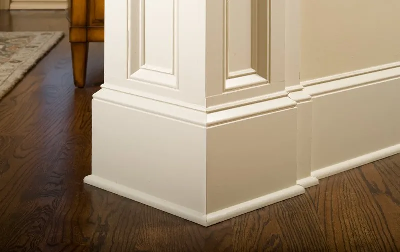 Wide white baseboard and column base on a wood floor
